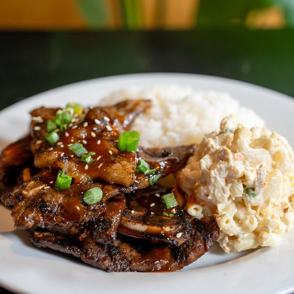 Grilled short ribs with sauce, sesame seeds, and green onions, served with white rice and macaroni salad.