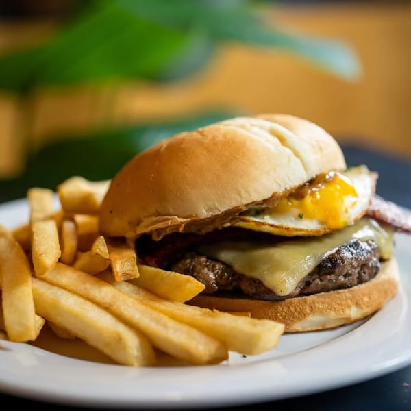 A Pasifika NW Grill & Bar burger with cheese and a fried egg, served with fries.