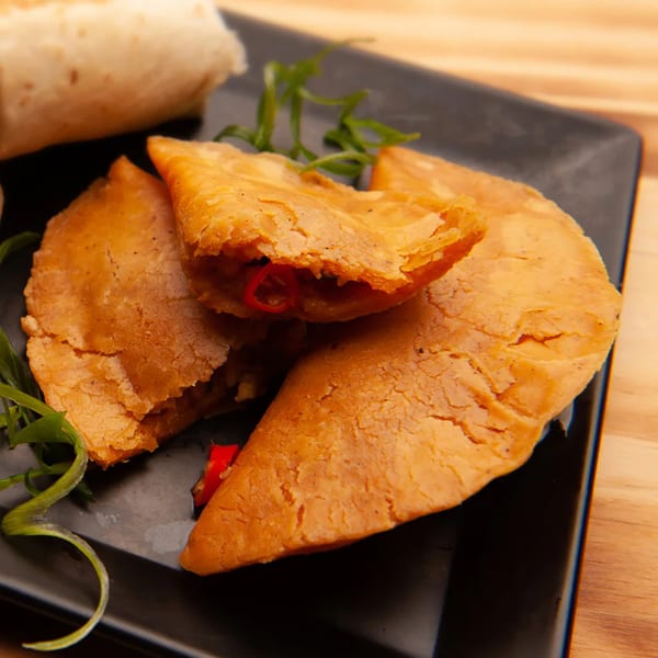 Golden-brown empanadas, one split open to reveal a savory filling with red peppers, on a black plate.