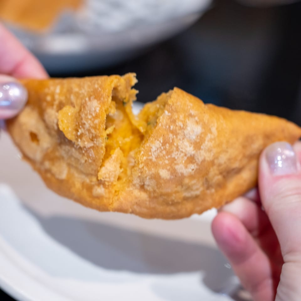 Hands holding a golden-brown, fried empanada, broken open to reveal a savory filling.