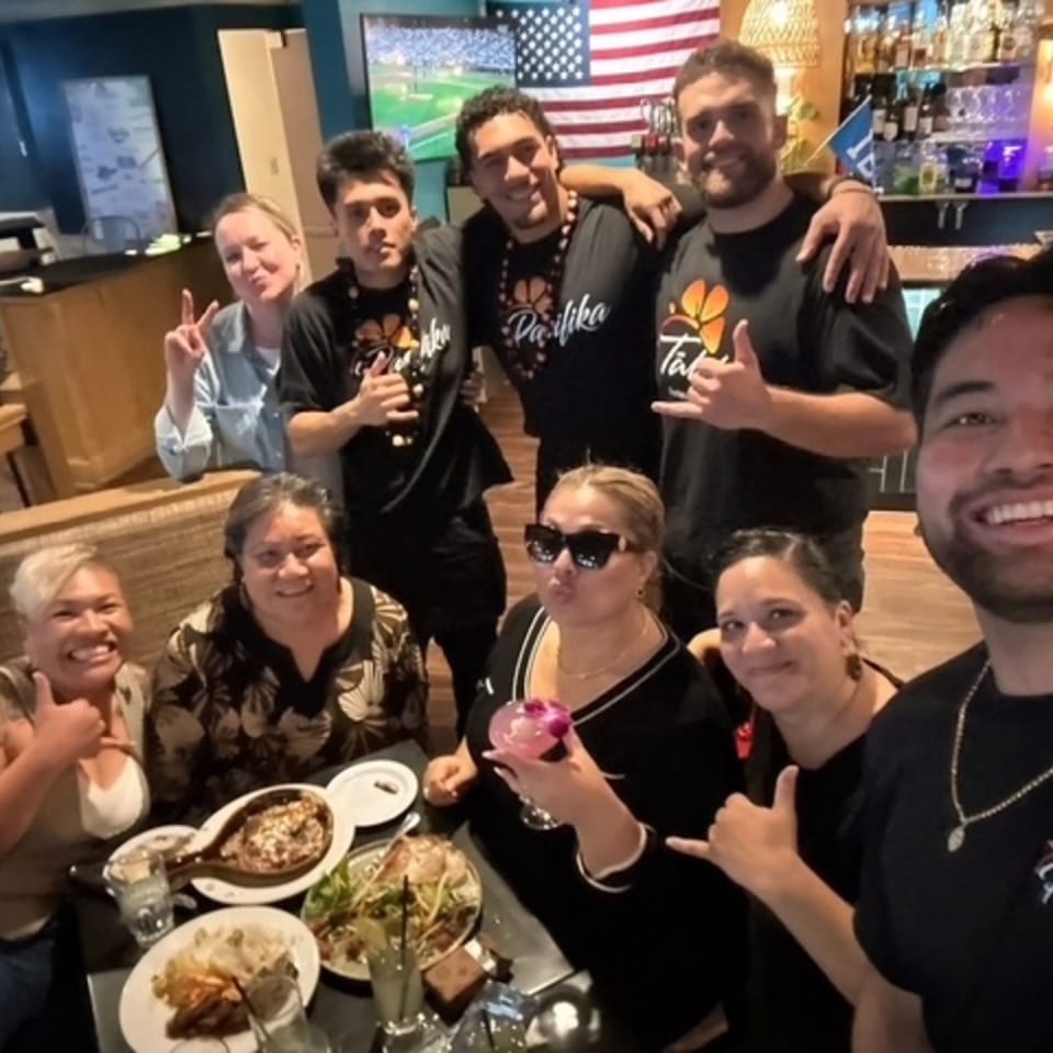 A group of people, some wearing black shirts with a flower logo, posing for a selfie in a restaurant.