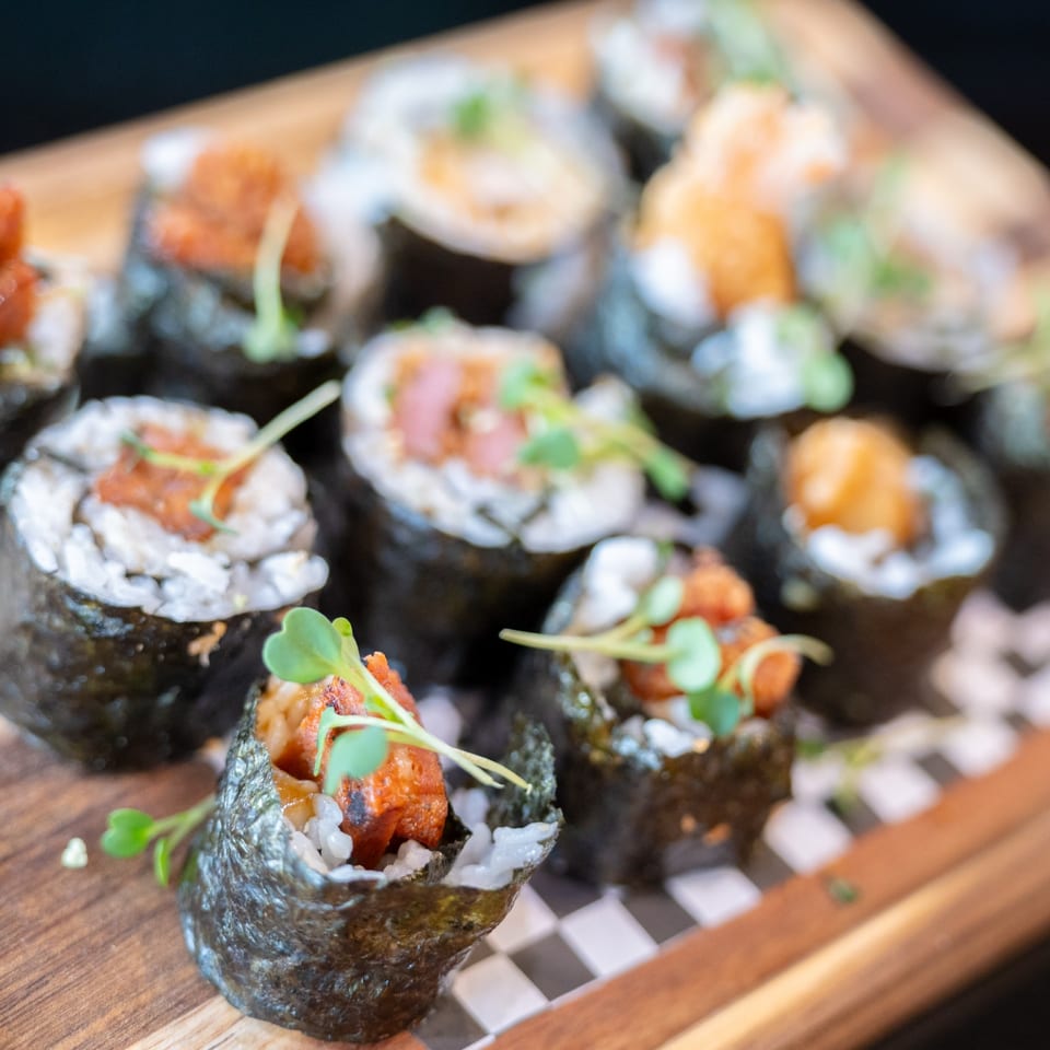 Close-up of sushi rolls with rice, seaweed, and various toppings, garnished with microgreens.